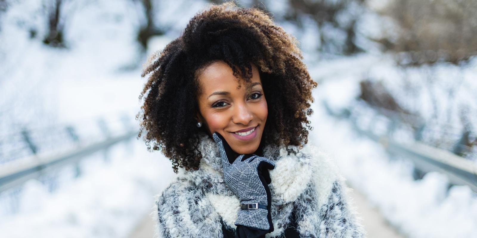 Woman with coily hair standing outside smiling during the wintertime